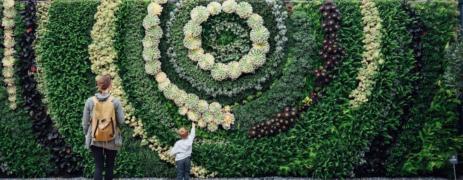 mother and child standing in front of a mural made of plants